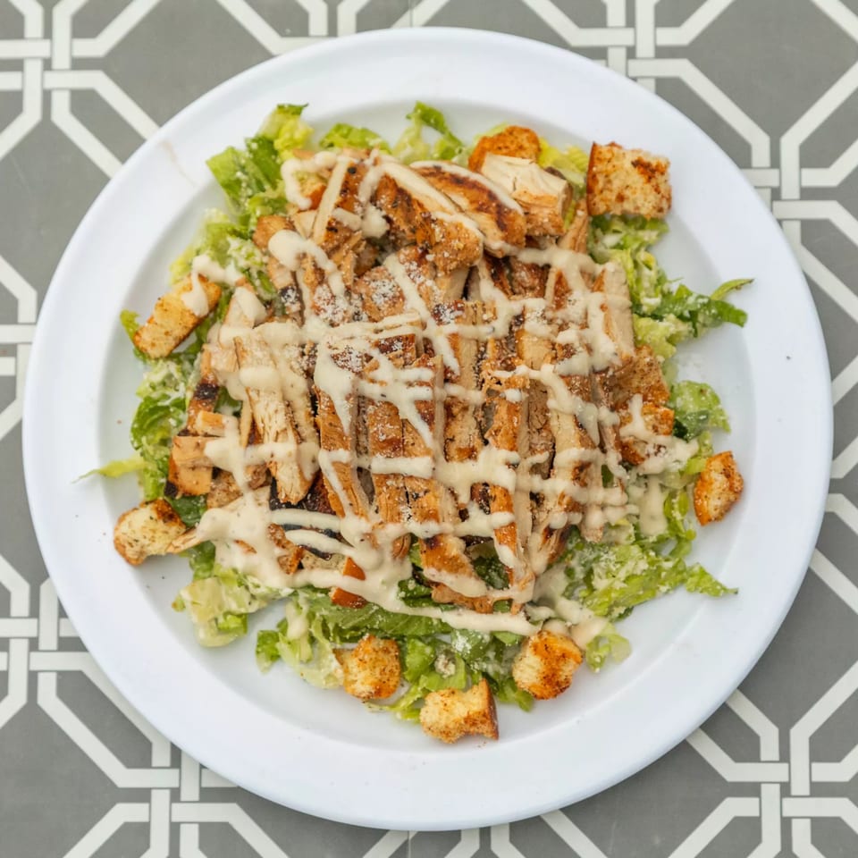 Overhead view of a Caesar salad with grilled chicken, croutons, and dressing on a white plate.