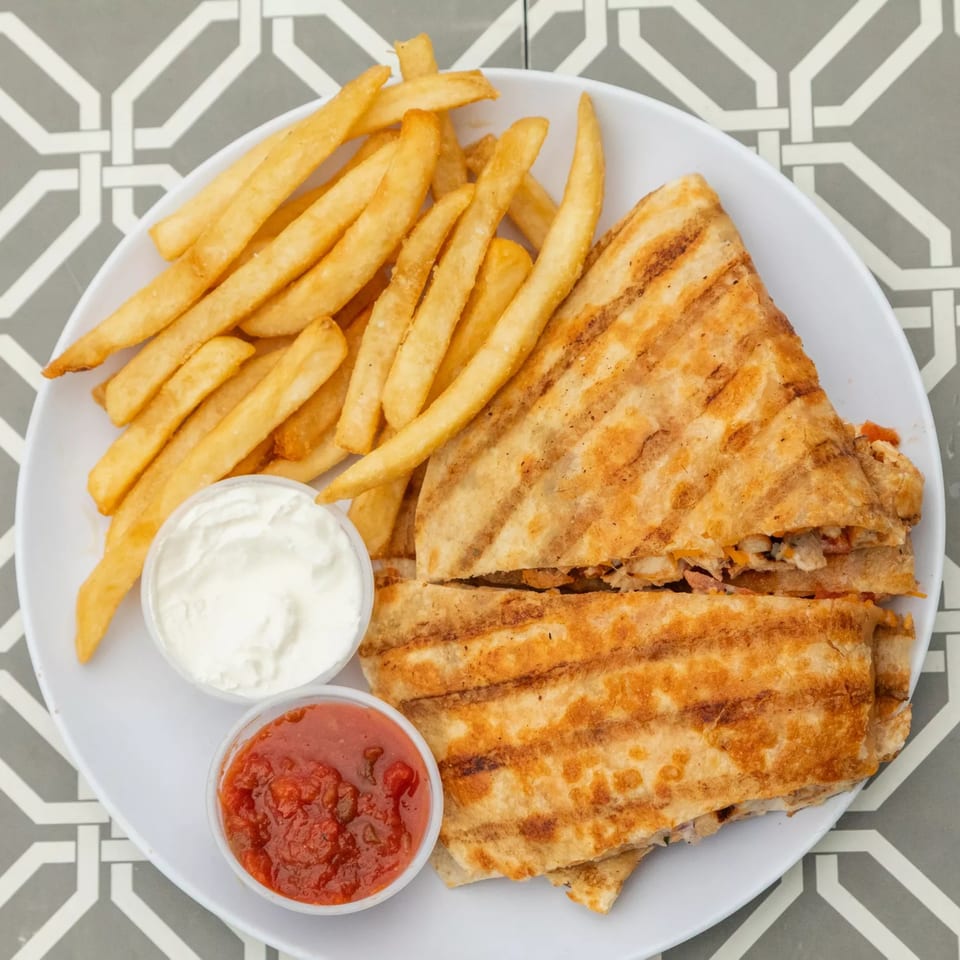 Grilled quesadilla with fries, salsa, and sour cream on a white plate at Island Social.
