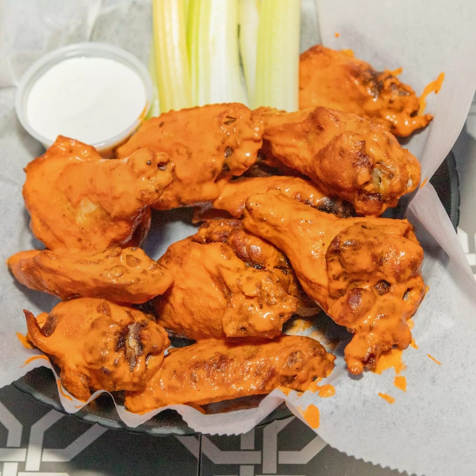A basket of Island Social's buffalo wings, with celery sticks and a side of ranch dressing.