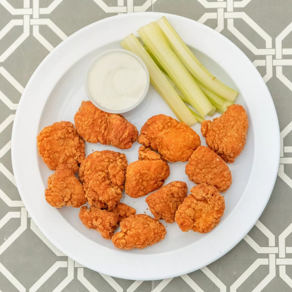 Crispy fried chicken nuggets with a side of celery sticks and ranch dressing on a white plate.