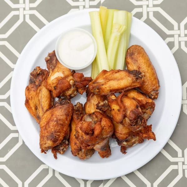 A white plate of crispy Island Social chicken wings with celery sticks and a side of ranch dressing.