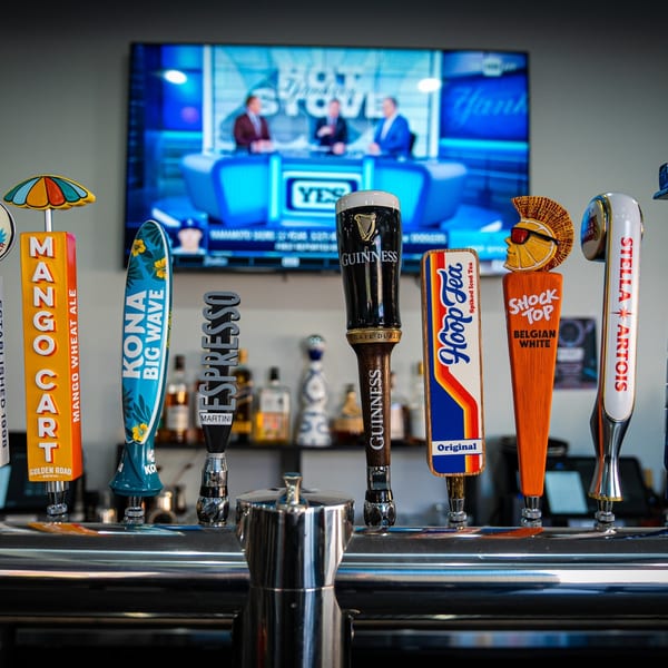 Close-up of beer taps at Island Social, with a TV showing a sports program in the background.
